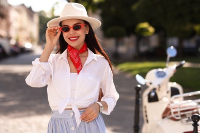 Photo of Smiling young woman in stylish hat and sunglasses on city street