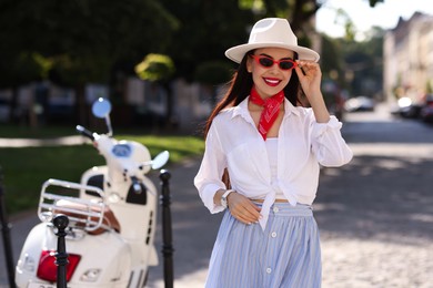 Smiling young woman in stylish hat and sunglasses on city street