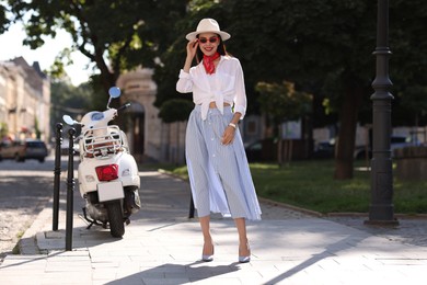 Smiling young woman in stylish hat and sunglasses on city street