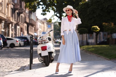 Smiling young woman in stylish hat and sunglasses on city street