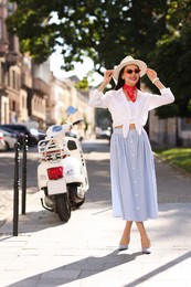 Photo of Smiling young woman in stylish hat and sunglasses on city street