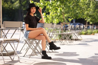 Beautiful young woman in stylish black hat on city street