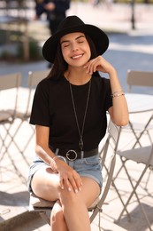 Photo of Beautiful young woman in stylish black hat on city street