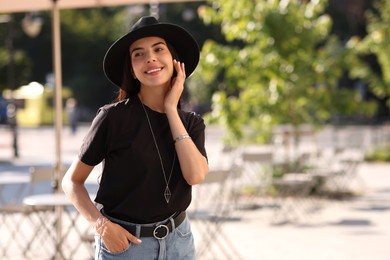 Photo of Beautiful young woman in stylish black hat on city street, space for text