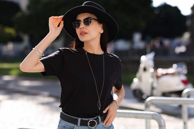 Young woman in stylish black hat and sunglasses on city street