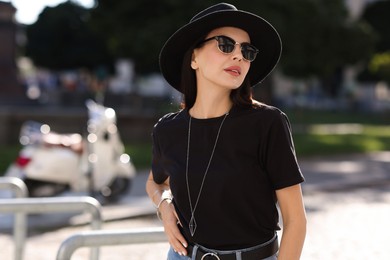 Young woman in stylish black hat and sunglasses on city street