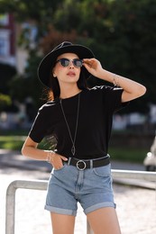 Photo of Young woman in stylish black hat and sunglasses on city street