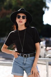 Young woman in stylish black hat and sunglasses on city street