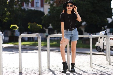 Photo of Young woman in stylish black hat and sunglasses on city street