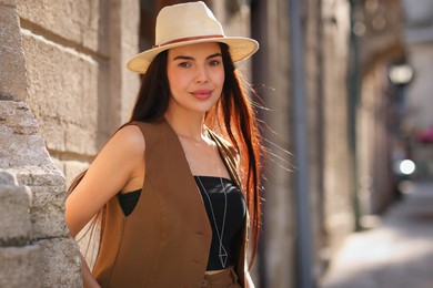 Photo of Beautiful young woman in stylish hat on city street, space for text