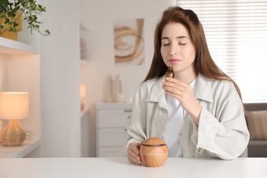 Photo of Woman with aroma diffuser and bottle of essential oil at home