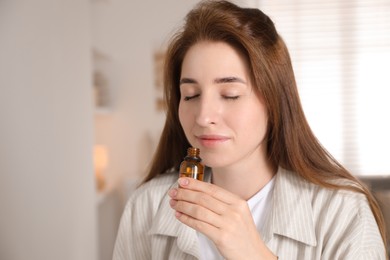 Photo of Woman with bottle of essential oil at home, space for text