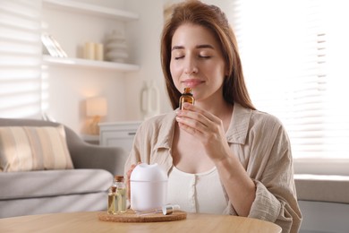 Photo of Woman with aroma diffuser and bottle of essential oil at home