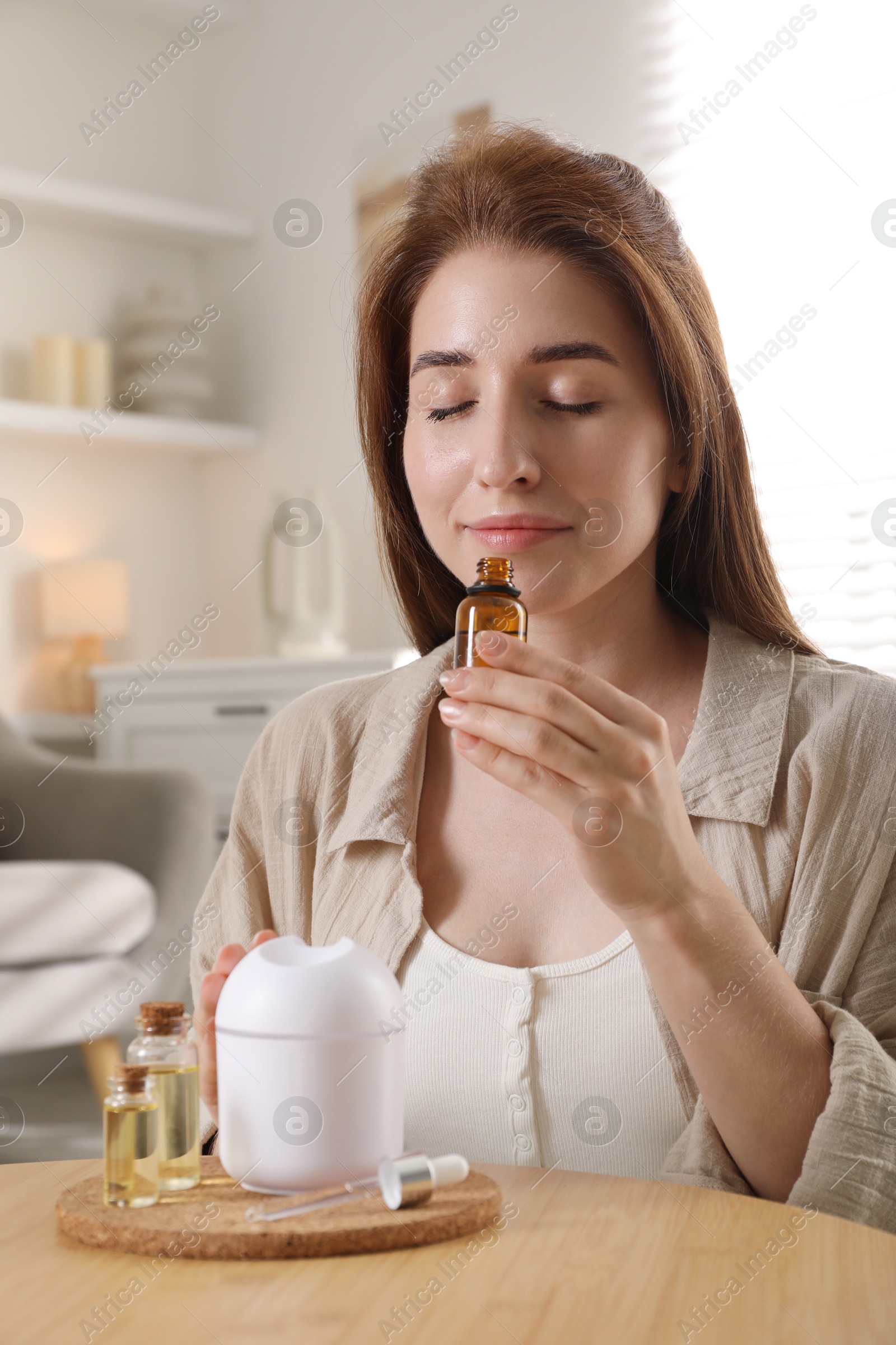 Photo of Woman with aroma diffuser and bottle of essential oil at home