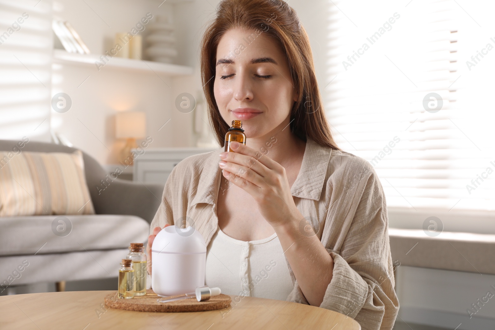 Photo of Woman with aroma diffuser and bottle of essential oil at home