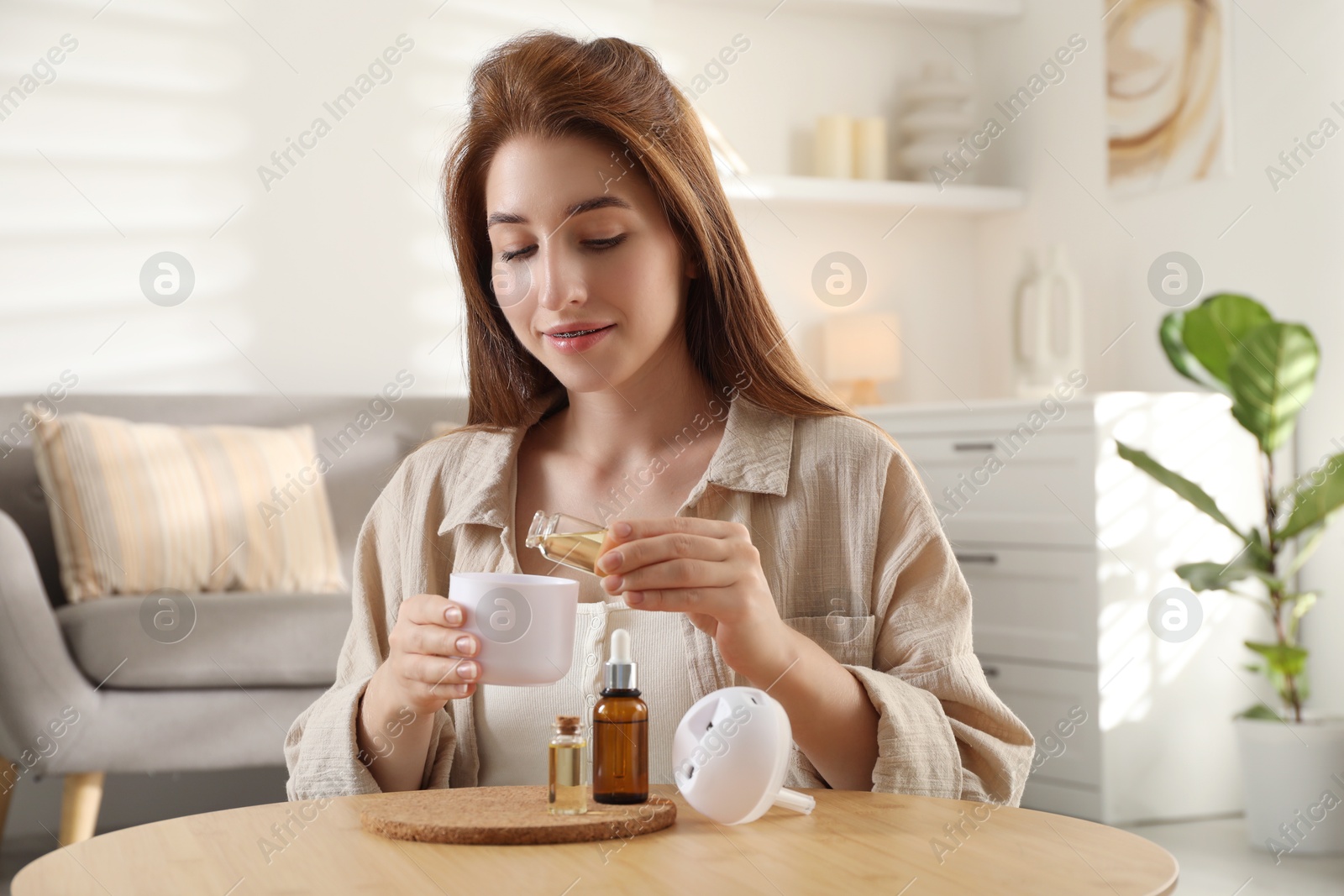 Photo of Woman adding essential oil to aroma diffuser at home