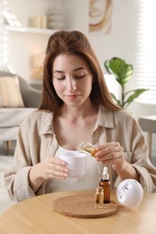 Photo of Woman adding essential oil to aroma diffuser at home