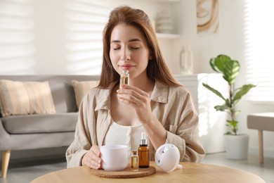 Photo of Woman with aroma diffuser and bottle of essential oil at home