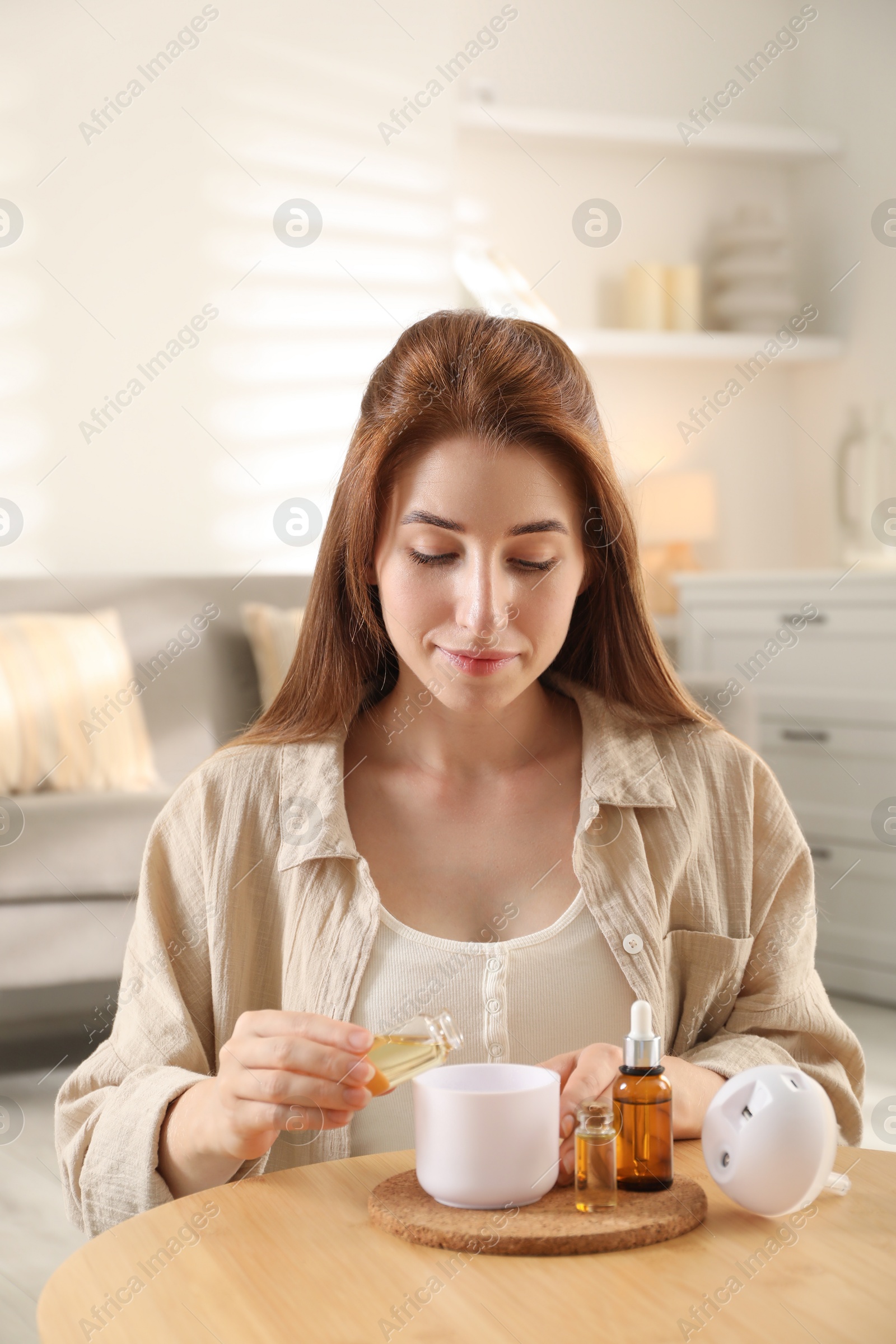 Photo of Woman adding essential oil to aroma diffuser at home