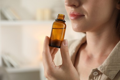 Woman with bottle of essential oil at home, closeup. Space for text