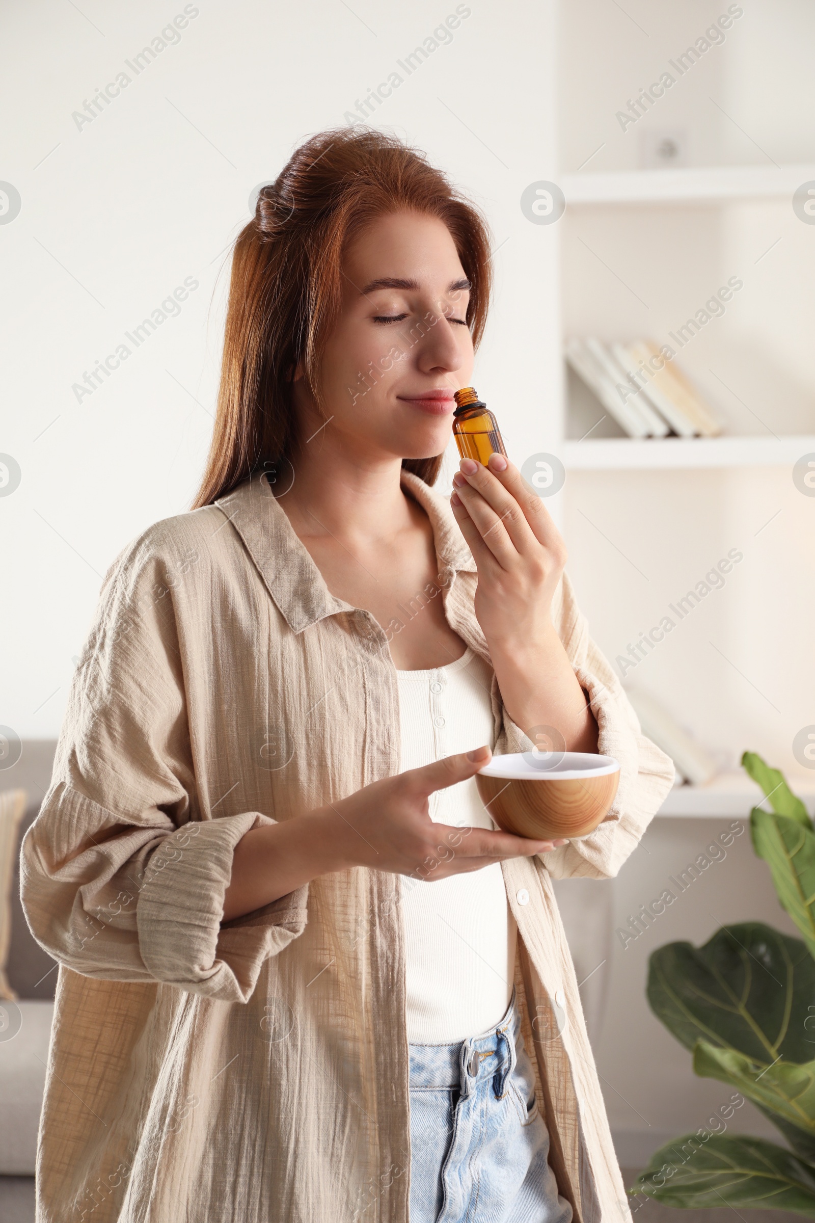 Photo of Woman with aroma diffuser and bottle of essential oil at home