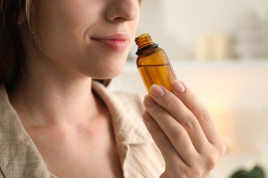 Woman with bottle of essential oil at home, closeup