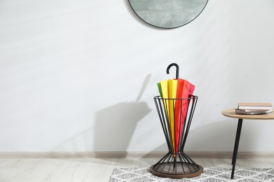 Photo of Colorful umbrella in stand near light wall. Space for text