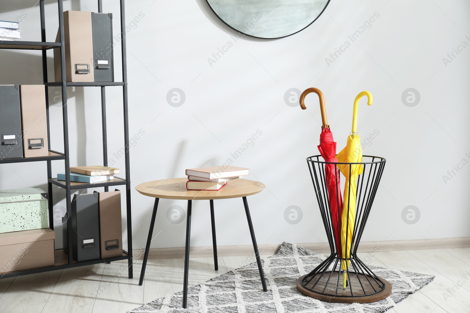 Photo of Colorful umbrella in stand, coffee table and shelving unit indoors