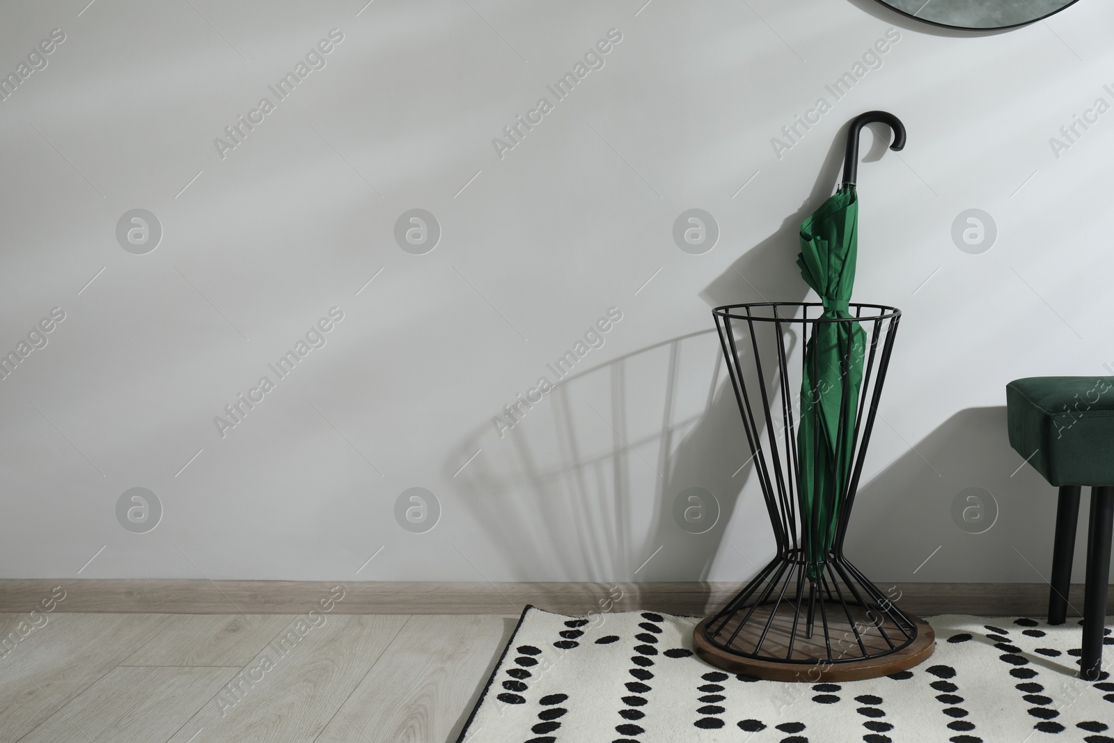 Photo of Green umbrella in stand near light wall. Space for text