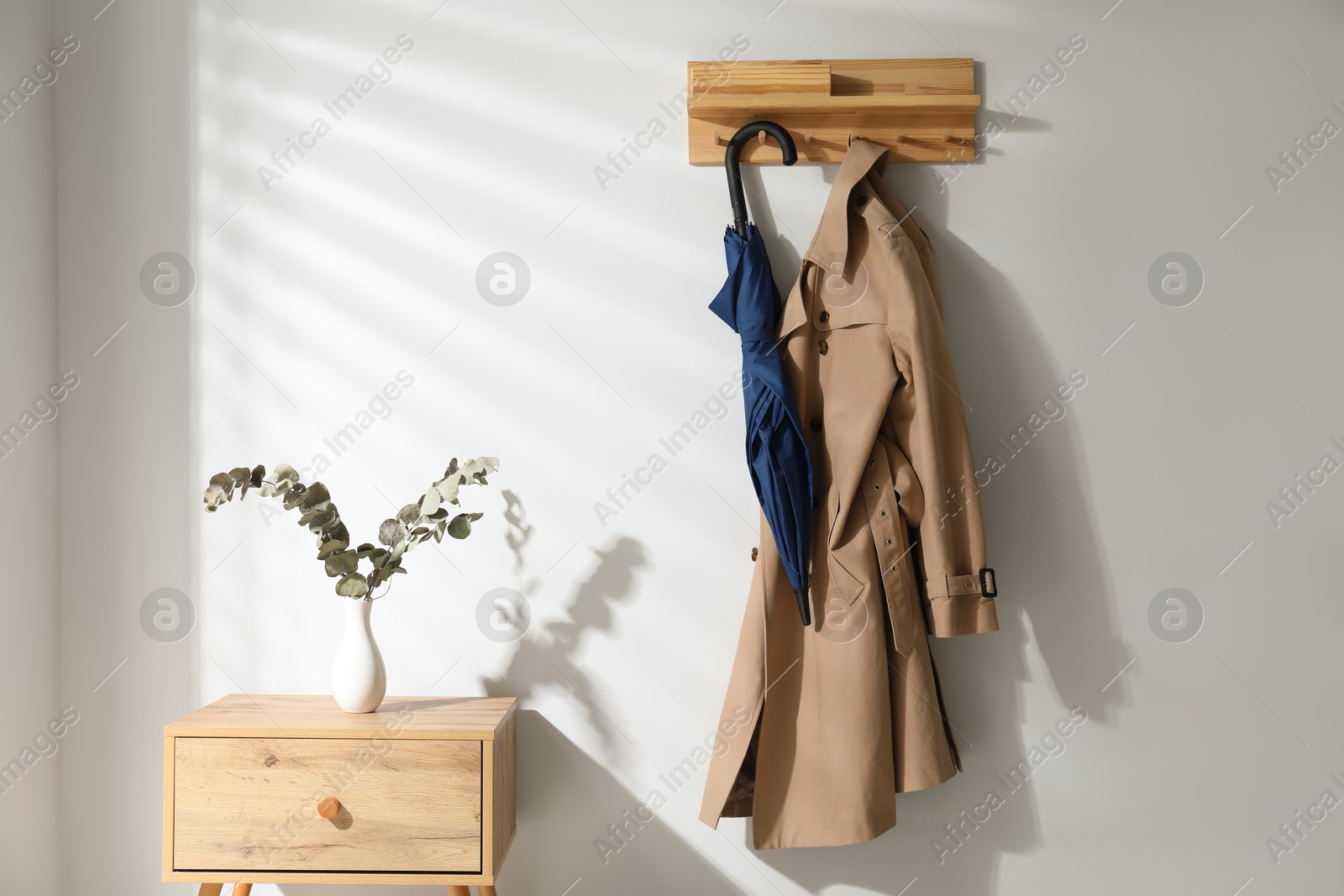 Photo of Colorful umbrella and trench coat hanging on rack at home