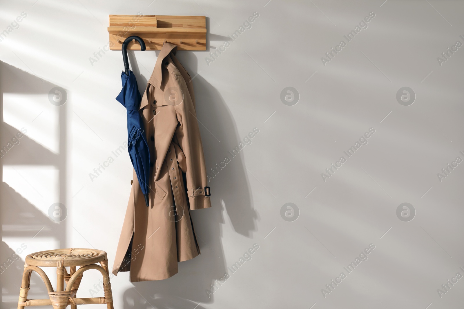 Photo of Colorful umbrella and trench coat hanging on rack at home. Space for text