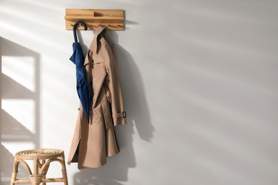 Photo of Colorful umbrella and trench coat hanging on rack at home. Space for text