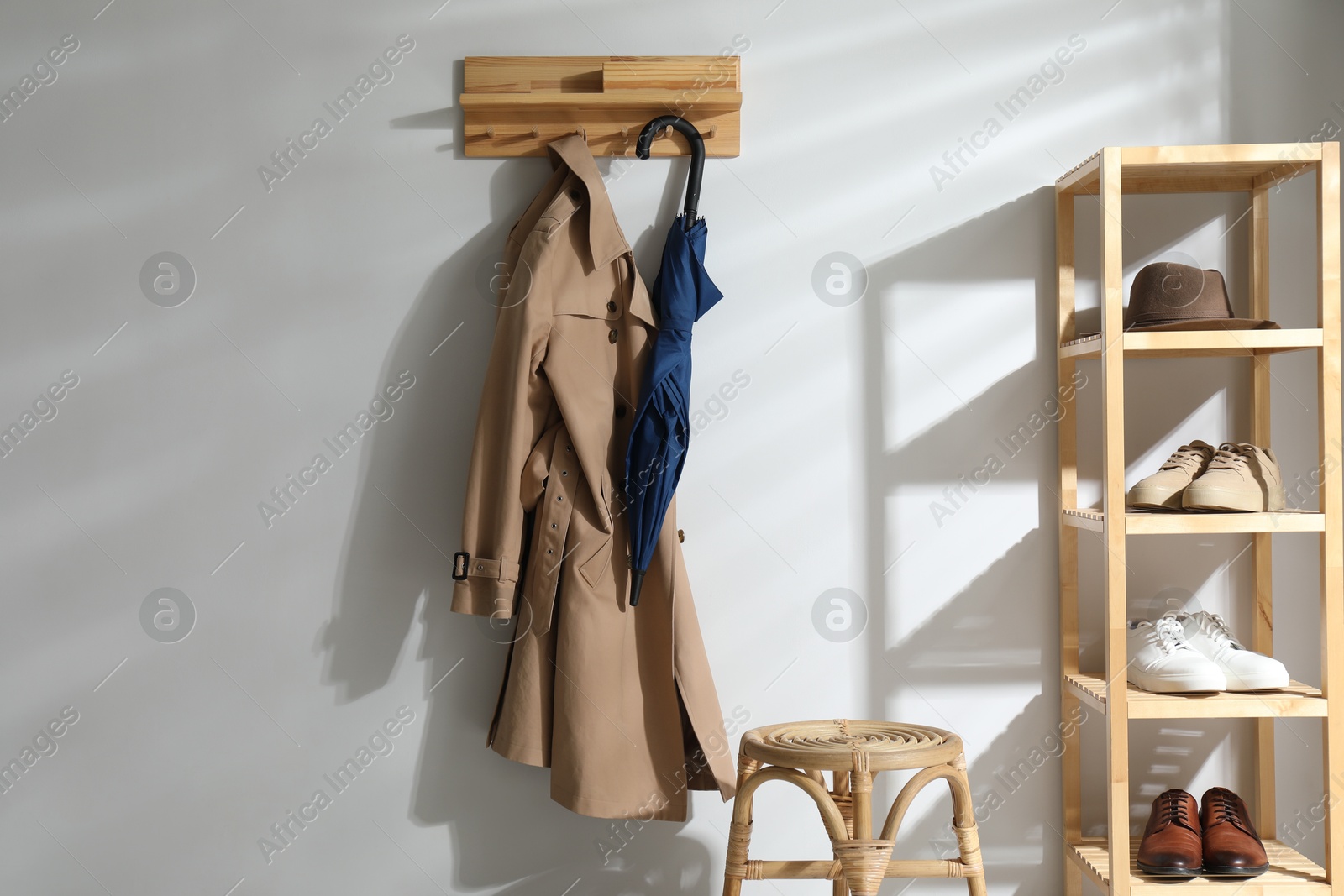 Photo of Colorful umbrella and trench coat hanging on rack at home