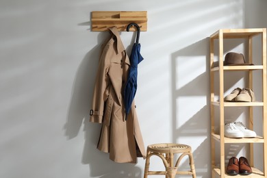 Photo of Colorful umbrella and trench coat hanging on rack at home