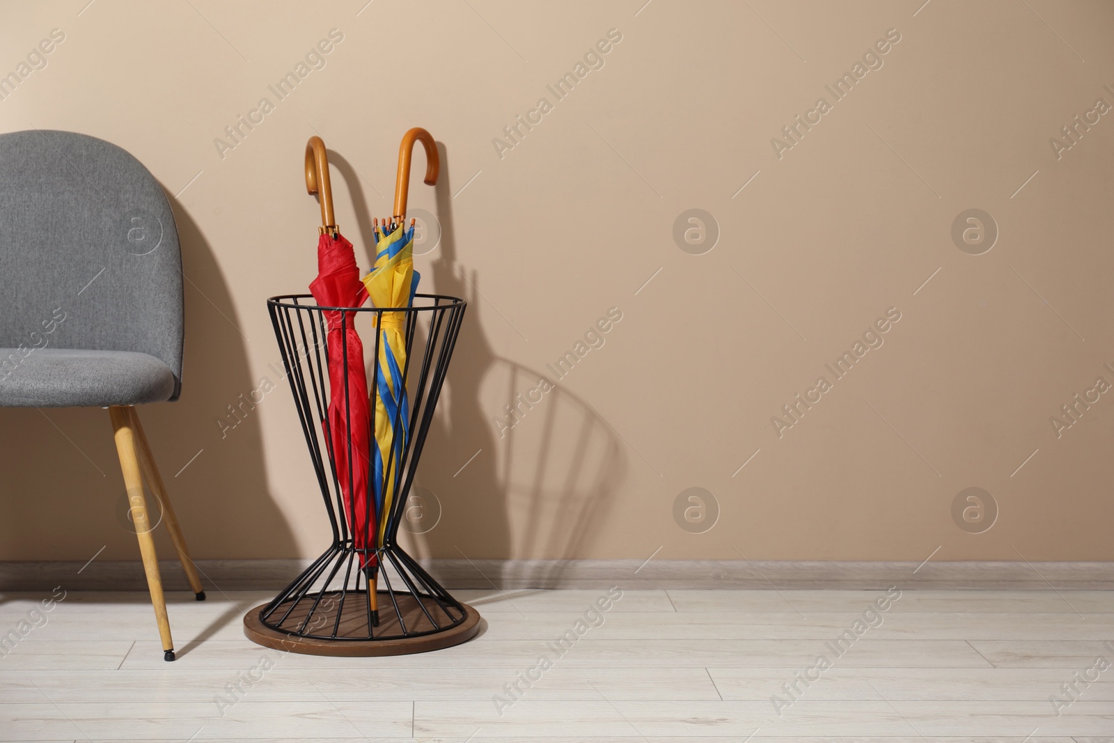 Photo of Holder with bright umbrellas and chair near beige wall. Space for text