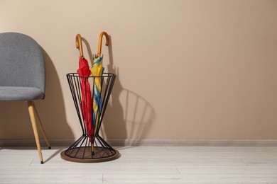 Photo of Holder with bright umbrellas and chair near beige wall. Space for text