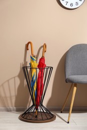 Holder with bright umbrellas and chair near beige wall