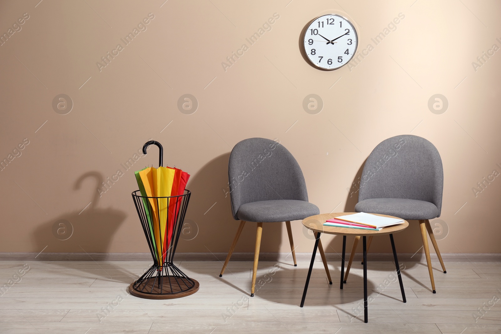 Photo of Bright umbrella in holder, coffee table and chairs near beige wall. Space for text