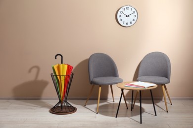 Bright umbrella in holder, coffee table and chairs near beige wall. Space for text