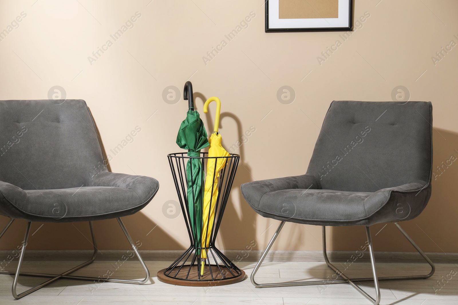 Photo of Bright umbrellas in holder and armchairs near beige wall