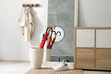 Holder with bright umbrellas, mirror and cabinets in hallway