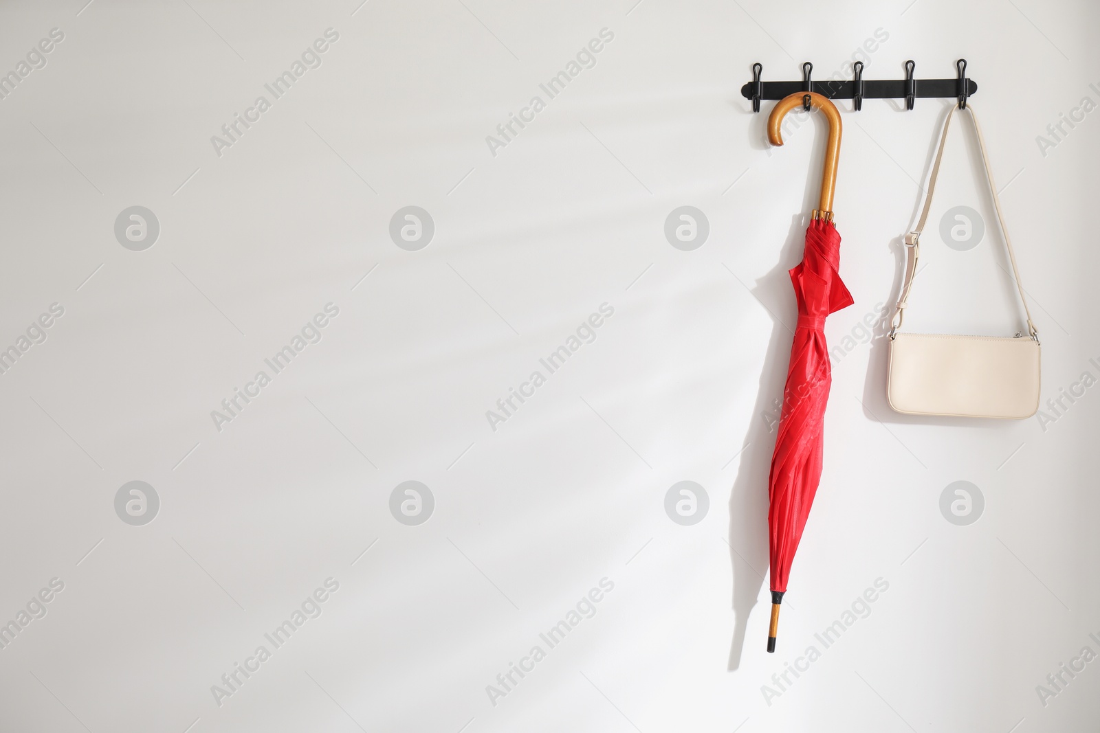 Photo of Red umbrella and bag on hanger near white wall. Space for text