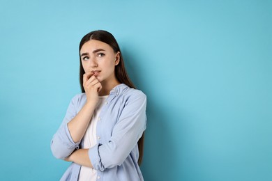 Portrait of scared woman on light blue background. Space for text