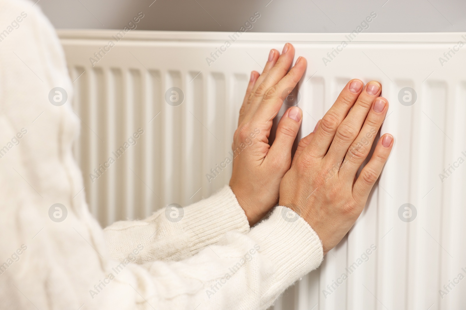 Photo of Woman warming hands near heating radiator at home, closeup