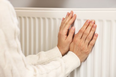 Woman warming hands near heating radiator at home, closeup