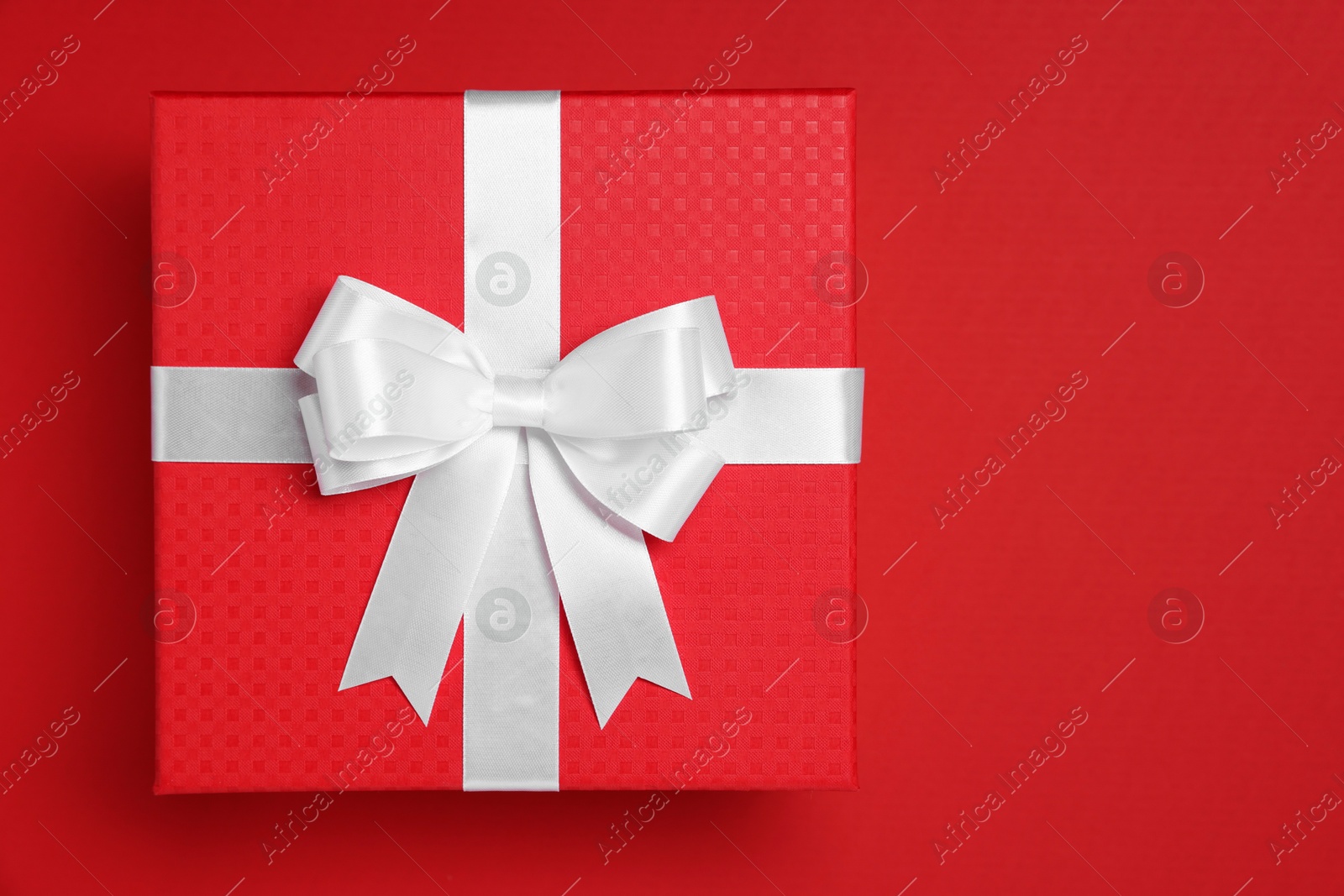 Photo of Gift box with white bow on red background, top view. Space for text