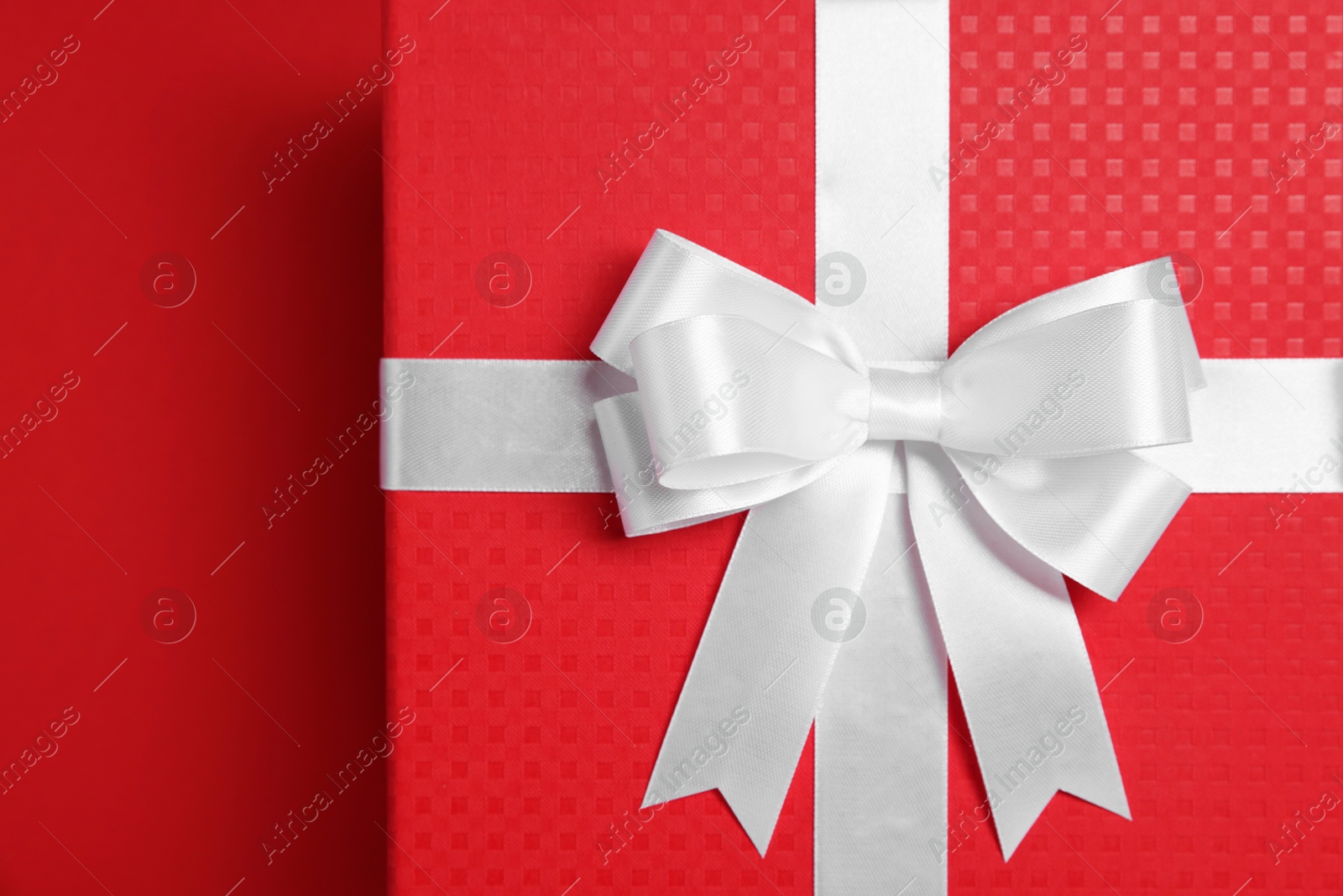 Photo of Gift box with white bow on red background, top view