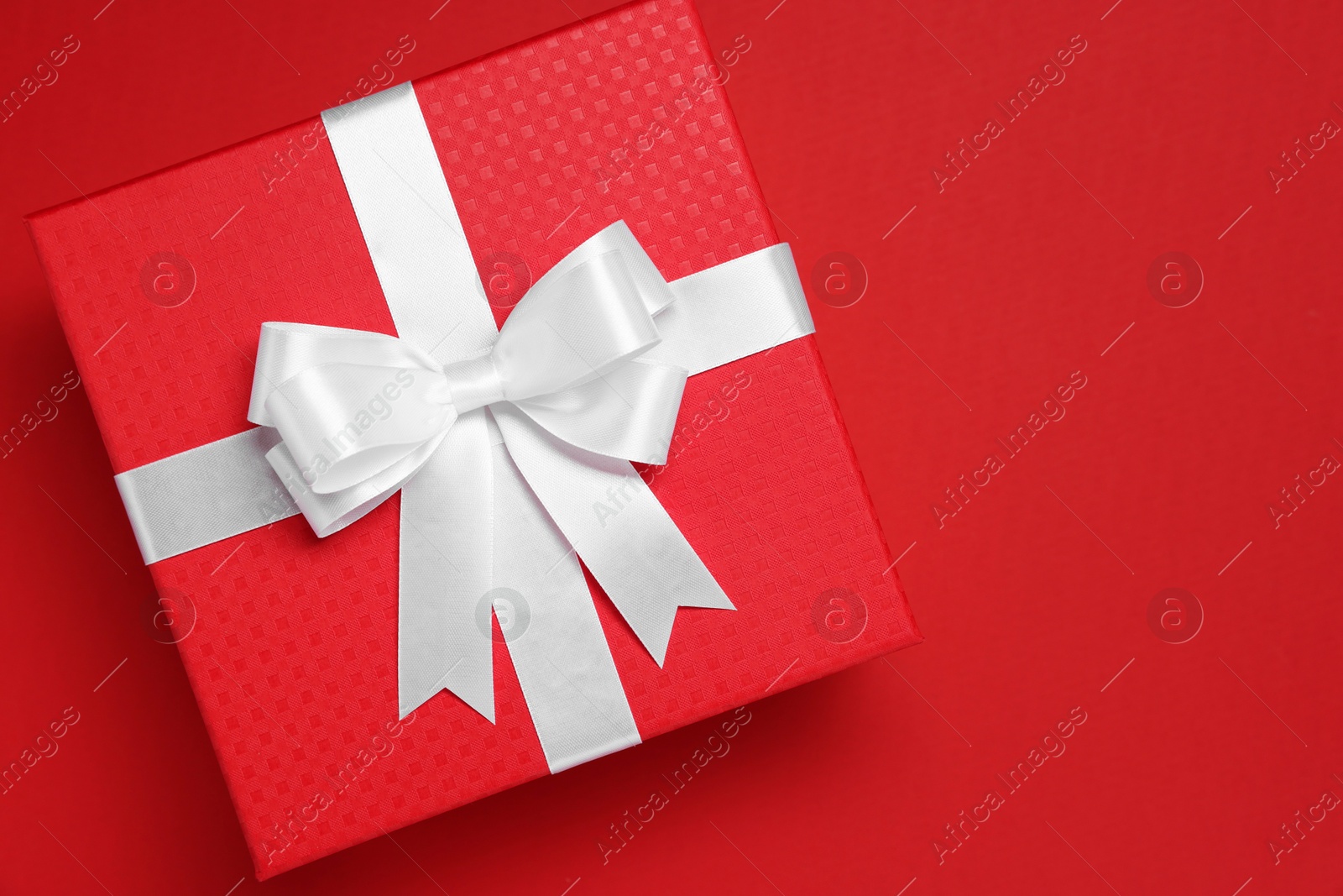 Photo of Gift box with white bow on red background, top view. Space for text