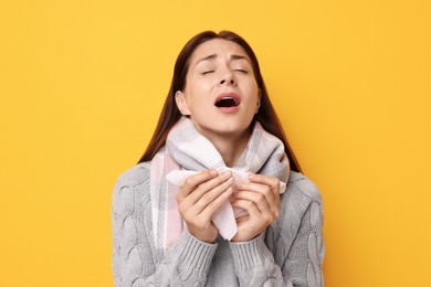 Sick woman with tissue sneezing on orange background. Cold symptoms