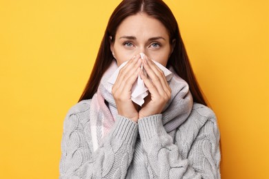 Sick woman with tissue on orange background. Cold symptoms